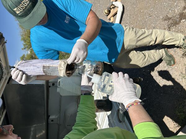 Two hydrologists transferring a collected microplastics sample into a jar. 