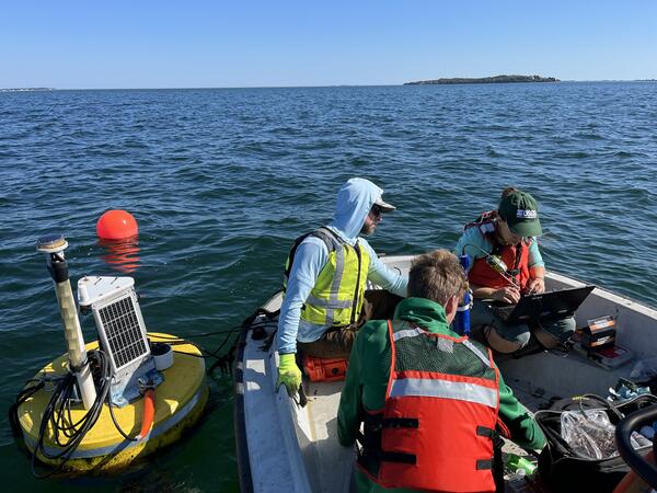 Three people sit in a boat surrounded by water and a buoy.