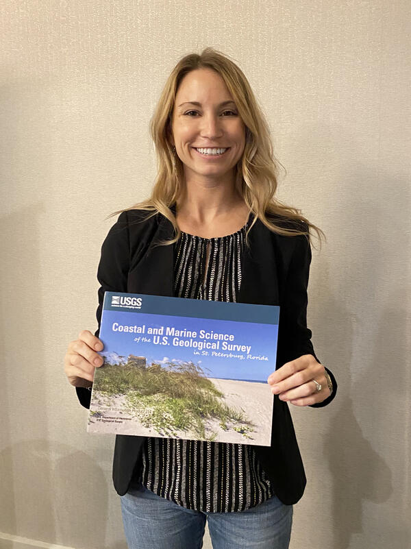 A woman stands with a booklet called, "Coastal and Marine Science of the USGS in St. Petersburg, Florida"