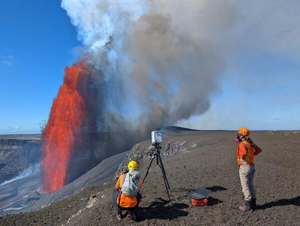 Color photograph of scientists measuring volcanic gas during eruption