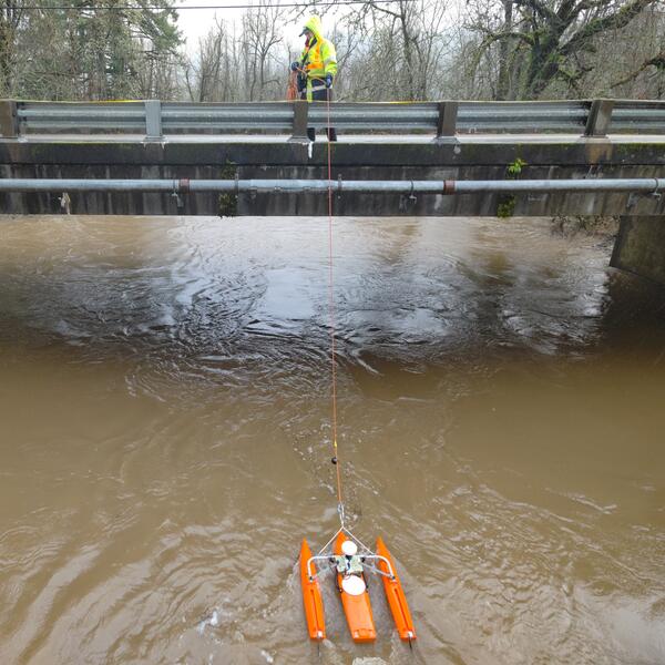 Female in safety gear pulls measurement equipment across the river from a bridge