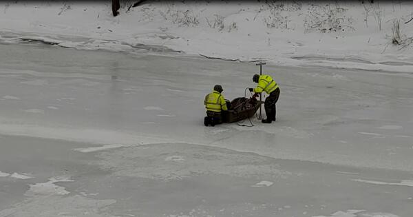 USGS Scientist standing on the frozen river lower equipment into the waters below through a hole in the ice