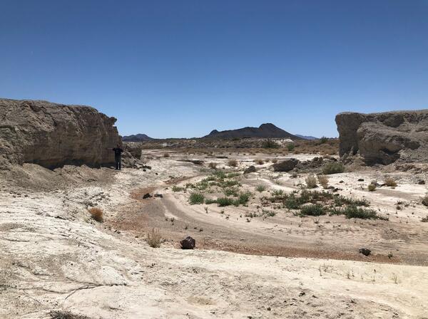 Dry desert landscape with rocky cliffs and sparse vegetation under a clear blue sky.