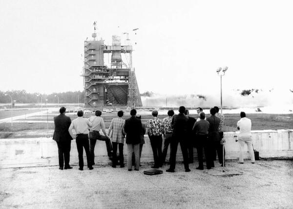 a group of men watch the first statis test-firing of the space shuttle main engine test in May 1975