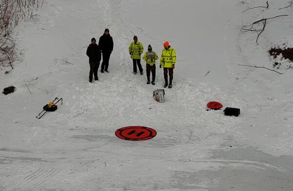 USGS scientists standing in the snow in front of an orange circular landing mat for their drone