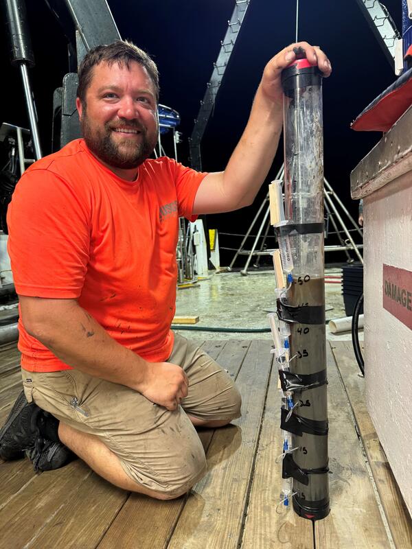 man kneeling on deck of ship next to a core sample at night