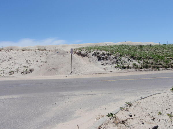 A dune that has sand washed over it next to a road during a storm