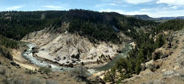Panorama of a river in a canyon flowing around a barren hillside with some gas vents