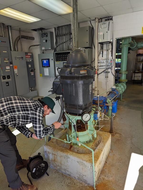 Man bent over lowering a measuring tape into an access pipe in a groundwater pump
