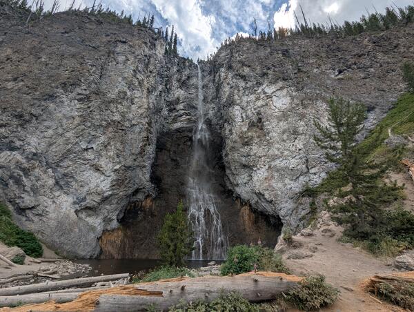 Ribbon-like waterfall on a gray cliff with a few trees and a splash pool in the foreground