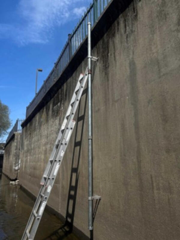 Steel pipe which monitors water level attached to the side of a bridge with a ladder next to it