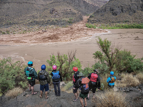 A river trip group watches a flash flood from the opposite bank of the Colorado River as it rushes down a canyon