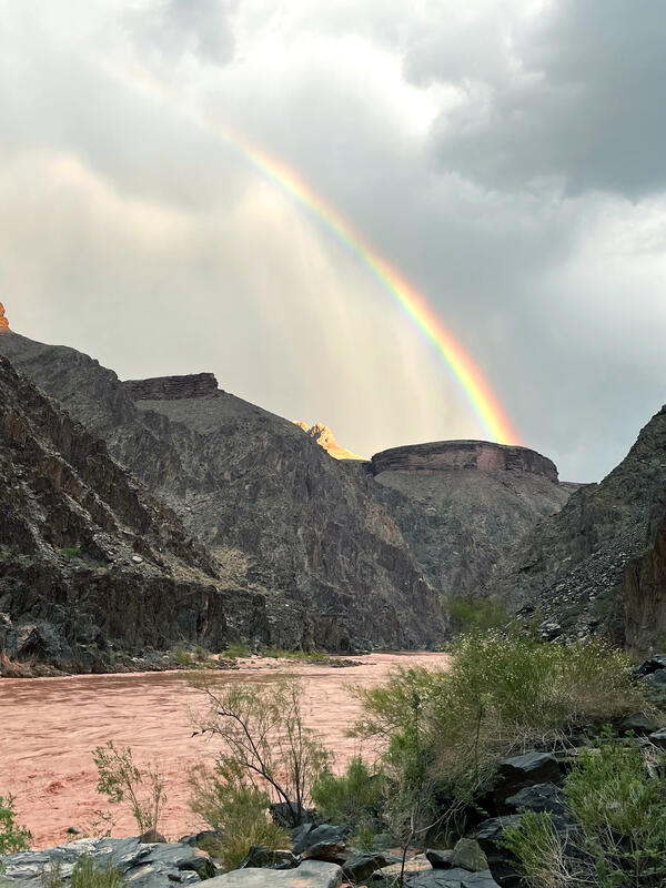 A rainbow in a stormy sky arches over Grand Canyon and the Colorado River