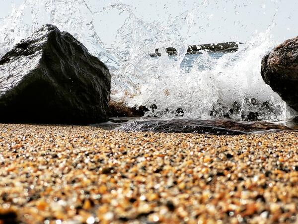A wave crashes between two rocks on a sandy beach.