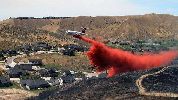 White airplane drops red fire retardant over the hills near a neighborhood
