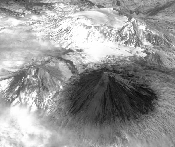 Satellite image of several large mountains, most snow-covered except the foreground volcano that's dark and covered in ash