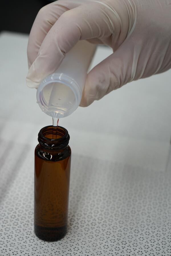 Close up view of gloved hand pouring water sample from plastic tube to glass bottle