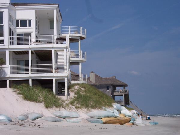 Sandbags partially shore up a badly eroded dune, exposed support columns of a beach home, NC
