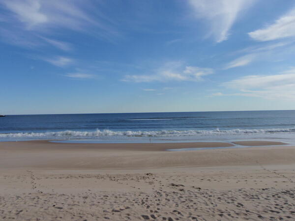 A calm sea with waves flowing onto the sand, forming a sandbar at the base of the beach