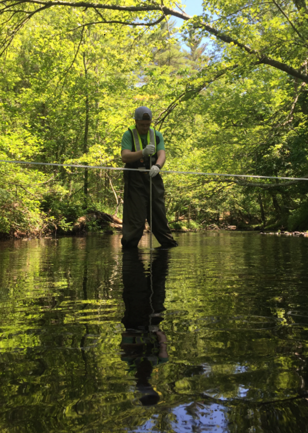 USGS scientist standing in a river collecting a water sample