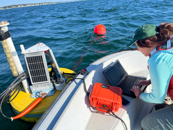 A woman types on her laptop on a boat next to a floating buoy.