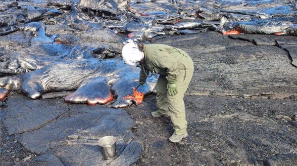 Color photograph of scientist collecting sample of lava