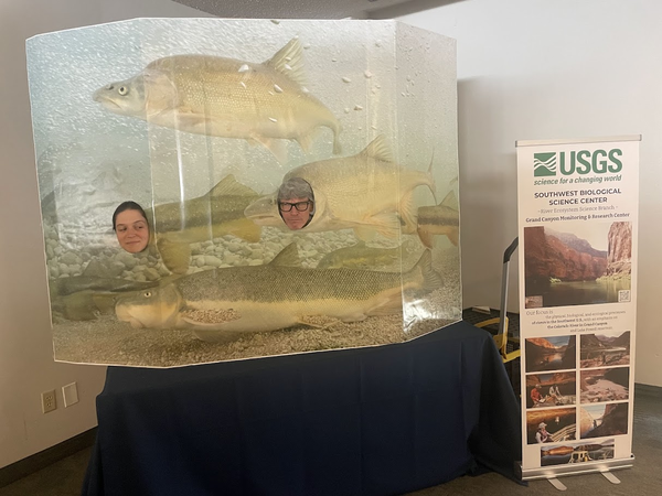 Two USGS scientists smile through a playful humpback chub cutout display