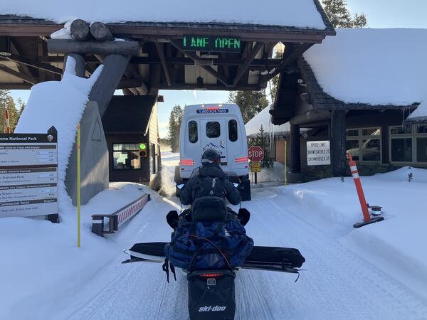 A person on a snowmobile waits behind an oversnow van at the park entrance station 