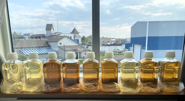Nine clear bottles filled with colored water samples ranging from light yellow to brown sitting on a windowsill