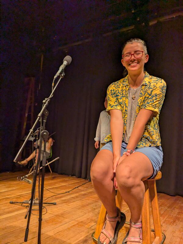 person sitting on stool next to microphone smiling