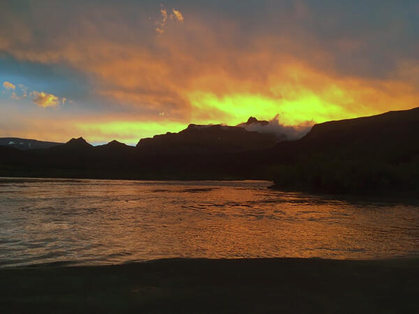 An orange, yellow and blue sunset reflects orange light on the Colorado River