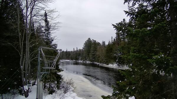 A gray metal cableway on the shore of a frozen river in winter