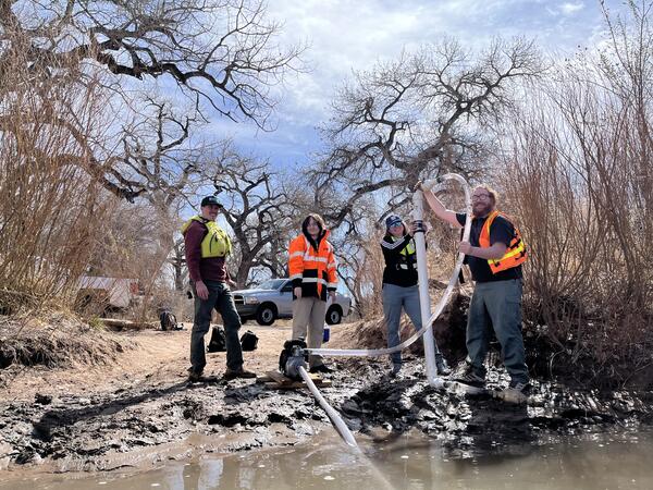 Four USGS employees stand on a riverbed, two of them holding a microplastics sampler. 