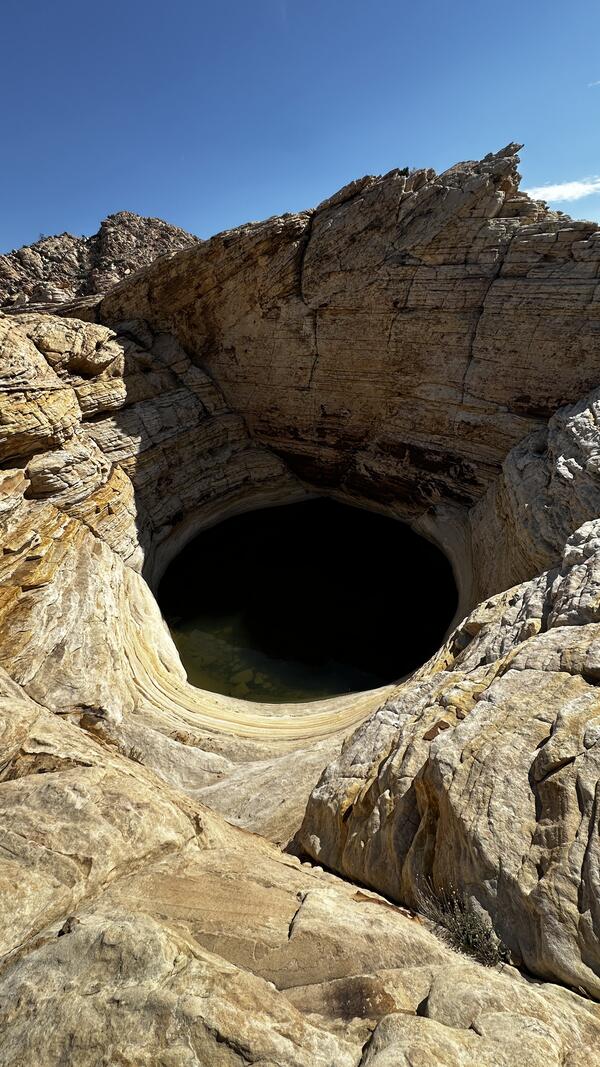 Round pool of water nestled among desert rocks beneath a clear blue sky.