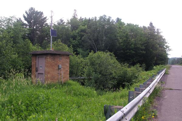 Brick streamgage house on bank of river next to rural country road in summertime
