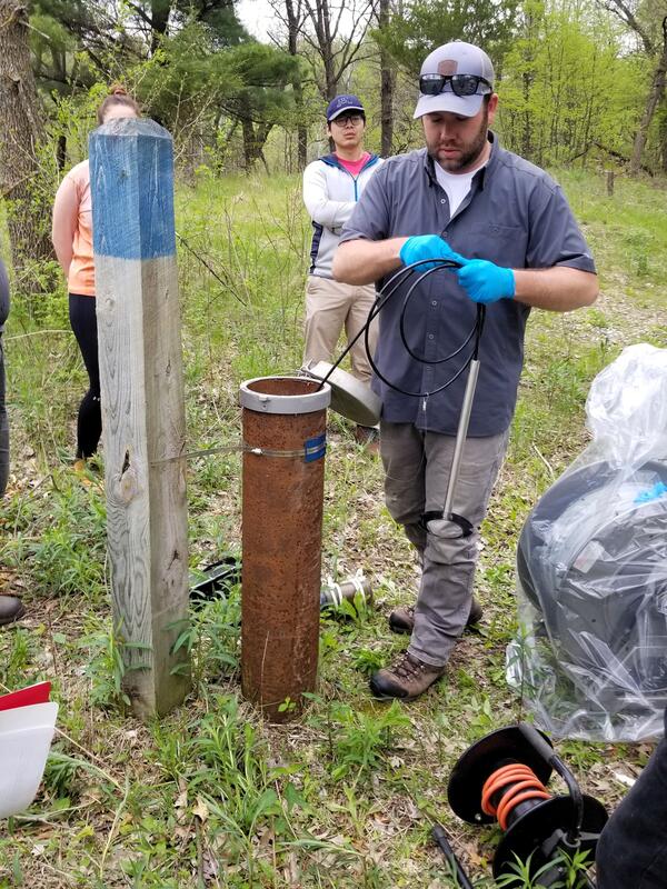 A man conducts a groundwater well monitoring demonstration in a grassy area