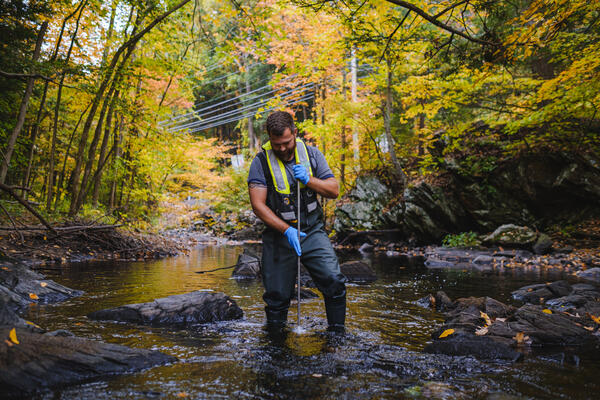 A man taking a water sample in a small river in the fall.