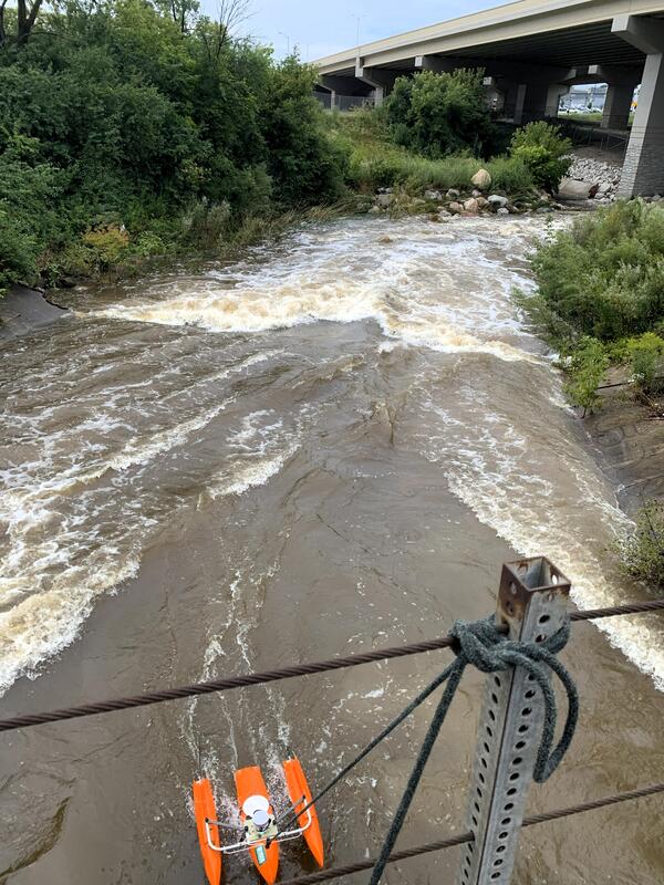 A bright orange acoustic Doppler current profiler takes a streamflow measurement in a flooded stream