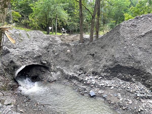 Clogged culvert pipe filled with sediment and some water running out of it.