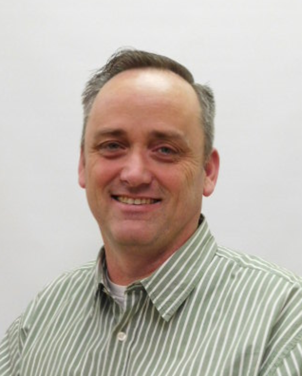 Photo of Vincent Delaney, dark hair with grey highlights, smiling, and wearing a collared shirt with green vertical pin stripes.