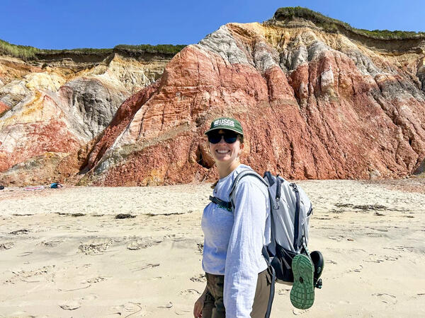Geographer and drone pilot stands in front of a colorful section of cliffs.