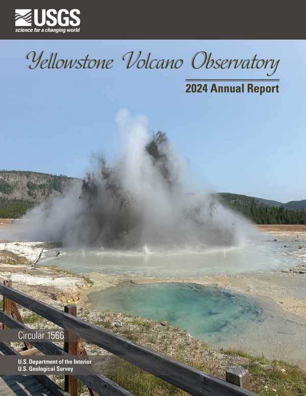 Muddy eruption from a blue water spring on barren ground, forested hills and blue sky in the background