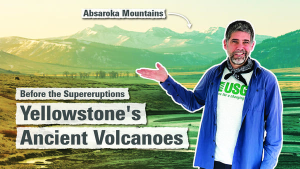 Man in blue shirt points to rugged snow-capped mountains in the background