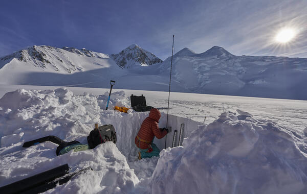 Person in a red jacket kneeling in a pit in the snow.