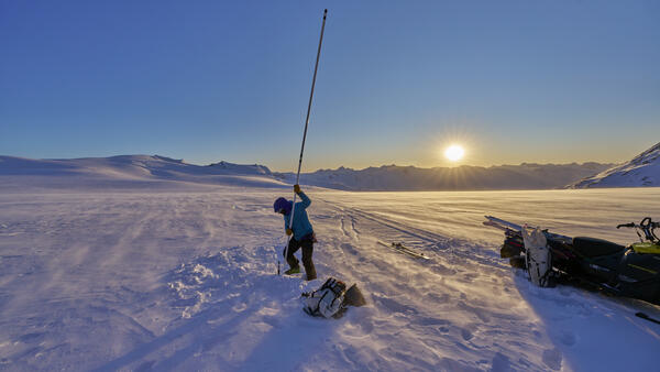 Person holding a lake stake vertically on a glacier.