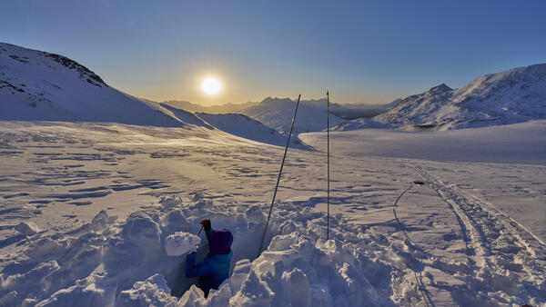 Snow pit on glacier with sun setting in background.