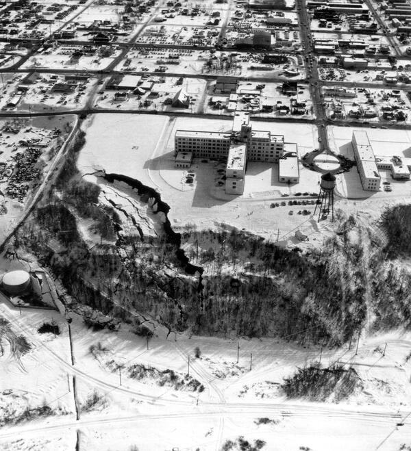 Snow covered ground with hospital, water tower and other buildings. Ground failure, cracking and sliding down slope.