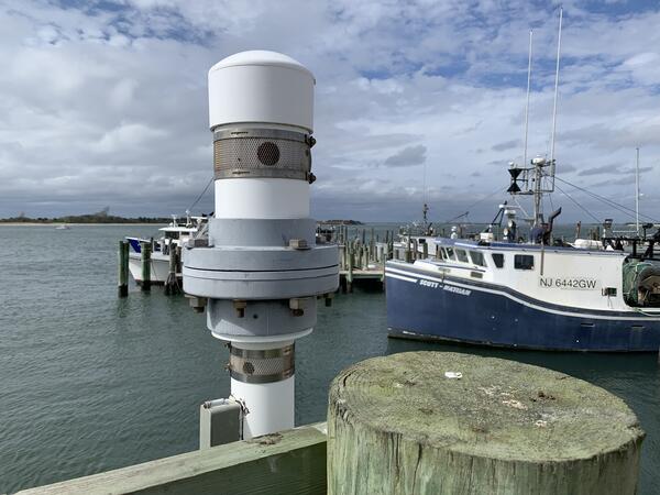 A white and grey cylindrical object with screened ventholes in its side sits atop a tube that reaches down into the bay below