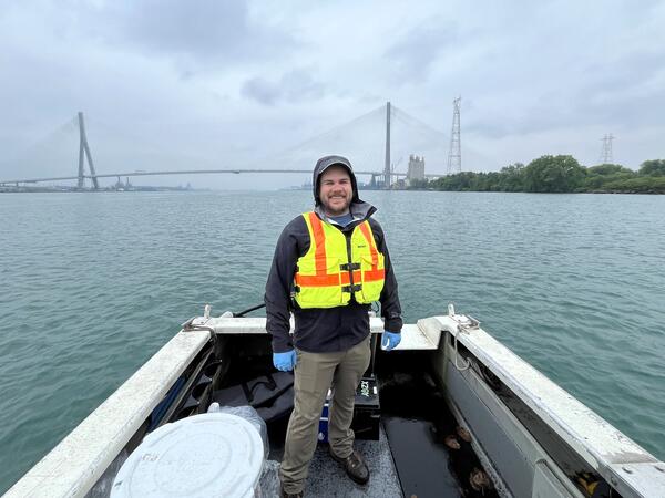 Man standing on boat with large bridge in background