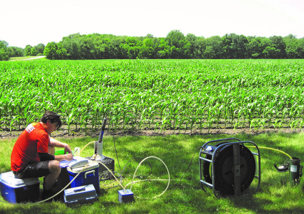 Scientist sits next to an agricultural field collecting water samples from a groundwater well.